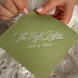 Op de afbeelding: Een vierkant, saliegroen papieren servet met een textuur, voorzien van de zilveren reli&euml;ftekst The Night Before en de namen EMMA & JORDAN in een kleiner, strak schreefloos lettertype dat eronder is gedrukt.