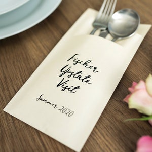May include: A white card with black calligraphy that reads "Fischer Upstate Visit Summer 2020". A fork and spoon are tucked into the card, and pink roses are in the background.