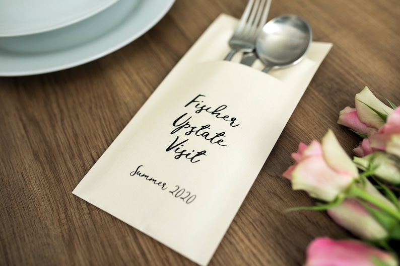 May include: A white card with black calligraphy that reads "Fischer Upstate Visit Summer 2020". A fork and spoon are tucked into the card, and pink roses are in the background.