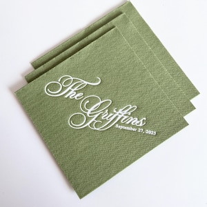 Peut inclure: Une pile de serviettes en papier carr&eacute;es vert sauge avec un texte blanc en relief indiquant The Griffins et la date du 27 septembre 2025. Les serviettes pr&eacute;sentent une surface textur&eacute;e et sont dispos&eacute;es en quinconce, l&eacute;g&egrave;rement d&eacute;cal&eacute;es.