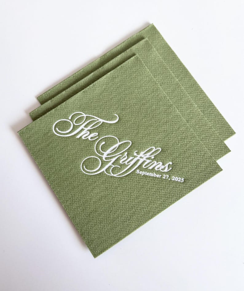 Peut inclure: Une pile de serviettes en papier carr&eacute;es vert sauge avec un texte blanc en relief indiquant The Griffins et la date du 27 septembre 2025. Les serviettes pr&eacute;sentent une surface textur&eacute;e et sont dispos&eacute;es en quinconce, l&eacute;g&egrave;rement d&eacute;cal&eacute;es.