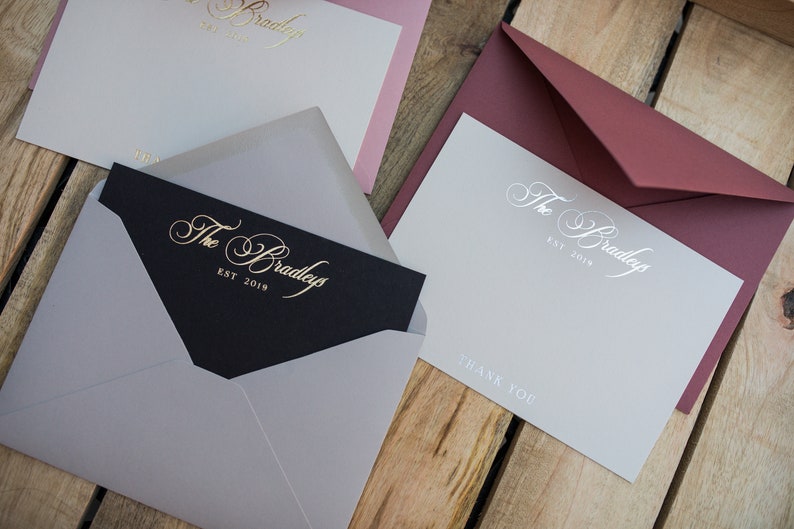 May include: Three stationery note cards with envelopes. The cards are white with a silver inscription that reads "The Bradleys Est. 2019" and "Thank You". The envelopes are burgundy, gray, and black.
