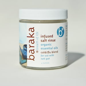 May include: A white jar with a brown label that reads "baraka *breath of life* infused salt rinse organic essential oils cold/flu blend for use with neti pot 4 ounces". The jar contains a clear liquid.