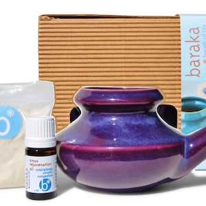 Op de afbeelding: Een paarse keramische neti pot, een klein flesje sinus verjongingsolie en een zakje mineraal zeezout. De artikelen zijn verpakt in een bruine kartonnen doos met de merknaam "baraka breath of life" en de tekst "sinus care kit" gedrukt op de zijkant. De kit bevat een neti pot, biologische sinus olie, mineraal zeezout.