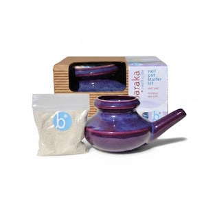 May include: A Baraka neti pot starter kit featuring a glossy purple ceramic neti pot with a spout, a clear plastic bag filled with white mineral sea salt, and a cardboard box labeled Baraka breath of life neti pot starter kit.