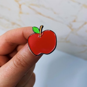 May include: A red enamel pin shaped like an apple with a green leaf and a brown stem.
