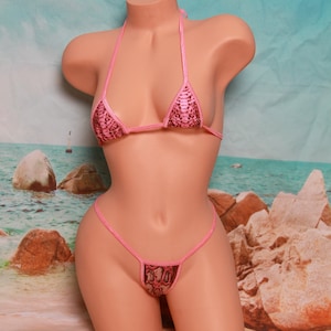 Puede incluir: Bikini rosa con estampado de piel de serpiente. La parte superior es de estilo triangular y la parte inferior es un bikini de hilo.
