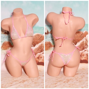 Puede incluir: Un bikini de color rosa y plata con purpurina y tirantes ajustables. La parte superior del bikini tiene forma triangular y la parte inferior es de estilo atrevido.