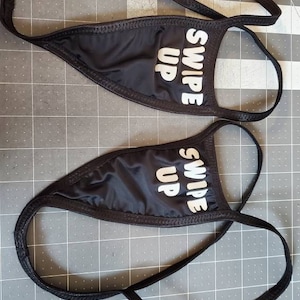 May include: Two black fabric garters with white text that reads "Swipe Up" on each. The garters are made of a soft, stretchy fabric and have a simple design.