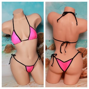 Puede incluir: Bikini rosa con ribetes negros. La parte superior es de estilo triangular con tirantes ajustables. La parte inferior es de estilo atrevido con lazos ajustables a los lados.