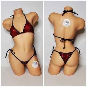 Puede incluir: Bikini rojo de lentejuelas con lazos negros. La parte superior del bikini tiene forma de triángulo y la parte inferior es de estilo coqueto. El bikini está en un maniquí.