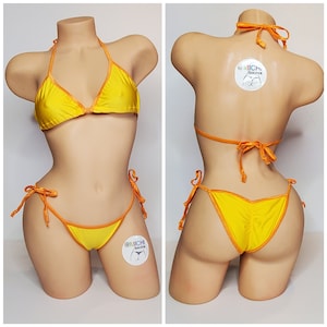 May include: A yellow bikini with orange trim. The bikini top is a triangle style with adjustable straps. The bikini bottom is a cheeky style with ties on the sides. The bikini is on a mannequin.