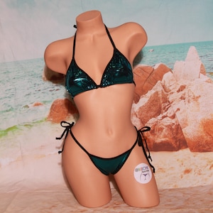 May include: A teal sequined bikini top and matching bottom with black trim. The bikini top has a halter style and the bottom is a tie-side style. The bikini is on a mannequin against a background of a beach scene.