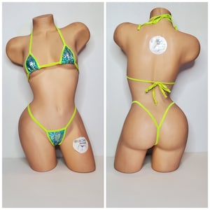 May include: A lime green and teal bikini with a small, iridescent, scale-like pattern. The bikini top is a triangle style with thin straps. The bikini bottom is a cheeky style with a thin strap on each side. The bikini is on a mannequin.