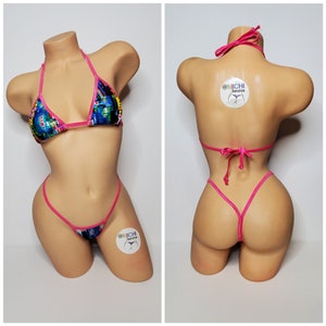 Puede incluir: Un bikini rosa y azul con un estampado abstracto colorido. La parte superior del bikini es de estilo triangular con tirantes finos. La parte inferior del bikini es de estilo atrevido con tirantes finos. El bikini está en un maniquí.