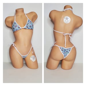 May include: White bikini with a blue and white floral print. The bikini top has a triangle shape and ties at the neck and back. The bikini bottom is a cheeky style with ties on the sides. The bikini is on a mannequin.