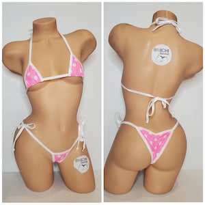 May include: Pink and white polka dot bikini with white straps and ties. The bikini top is a triangle style and the bottom is a cheeky style. The bikini is made by @Michi Bikinis.