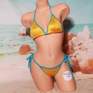 May include: A yellow satin bikini with turquoise trim. The bikini top is a triangle style with adjustable straps. The bikini bottom is a cheeky style with ties on the sides. The bikini is on a mannequin against a beach background.