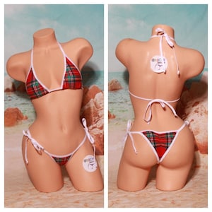 Puede incluir: Bikini de cuadros rojos y verdes con ribetes blancos. La parte superior e inferior del bikini están atadas con cordones blancos. El bikini está en un maniquí sobre un fondo de playa.