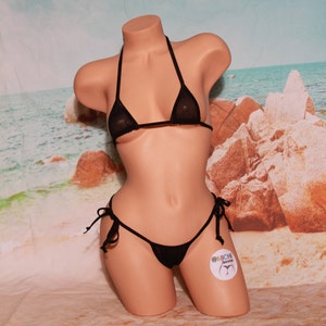 以下が含まれることがあります： 細いストラップが付いた黒い透き通ったメッシュのビキニトップとボトム。ビキニはビーチの背景に置かれたマネキンに着せられています。