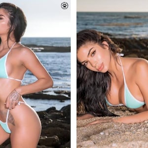 May include: A woman in a turquoise bikini with white trim poses on a rocky beach. The sea is in the background.