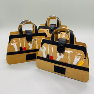 May include: Three brown paper tool bag gift boxes with black handles and black accents. Each box has a variety of tools printed on the front, including wrenches, screwdrivers, a hammer, a saw, and a pencil.