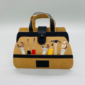 K&ouml;nnte beinhalten: Eine braune Papiertasche f&uuml;r Werkzeug mit einem schwarzen Griff und einer schwarzen Klappe. Die Tasche ist gef&uuml;llt mit verschiedenen Werkzeugen, darunter Schraubenschl&uuml;ssel, Schraubendreher, ein Hammer, ein Bleistift und eine S&auml;ge.