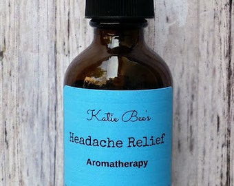 May include: A brown glass aromatherapy spray bottle with a black cap and a light blue label. The label reads "Katie Bee's Headache Relief Aromatherapy" and lists ingredients. The bottle contains 2 oz of product.