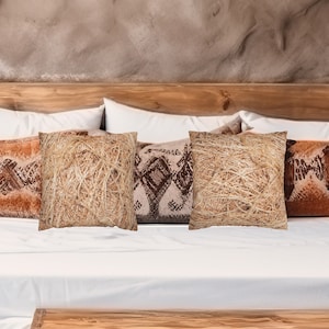 May include: Three decorative throw pillows with a natural fiber texture. The pillows are arranged on a white bed with a wooden headboard. The pillows are in a neutral color palette of beige and brown.