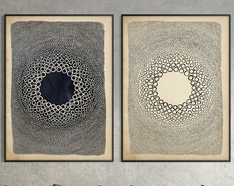 以下が含まれることがあります： 黒と白の円形模様が描かれた抽象的なアートプリントが2枚、額装されています。プリントは、グレーの壁に、グレーのソファとクッションの上に飾られています。