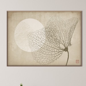 Op de afbeelding: Een beige en bruine wandkunstprint met een gestileerde afbeelding van een delicaat, skeletachtig blad met een witte cirkel op de achtergrond. De print is ingelijst en hangt aan een witte muur boven een houten consoletafel.