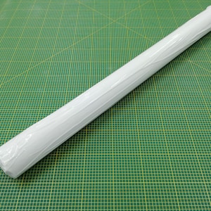 May include: A white roll of paper wrapped in clear plastic, sitting on a green cutting mat with yellow grid lines.