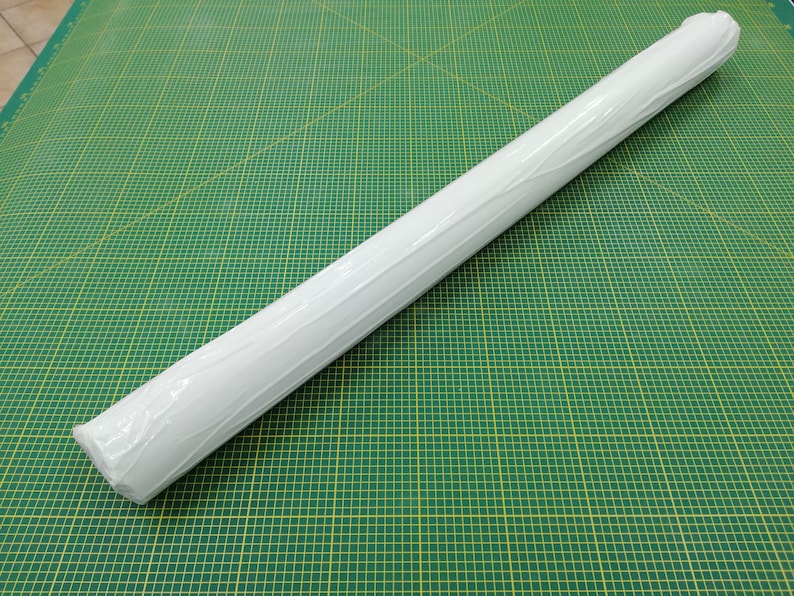 May include: A white roll of paper wrapped in clear plastic, sitting on a green cutting mat with yellow grid lines.