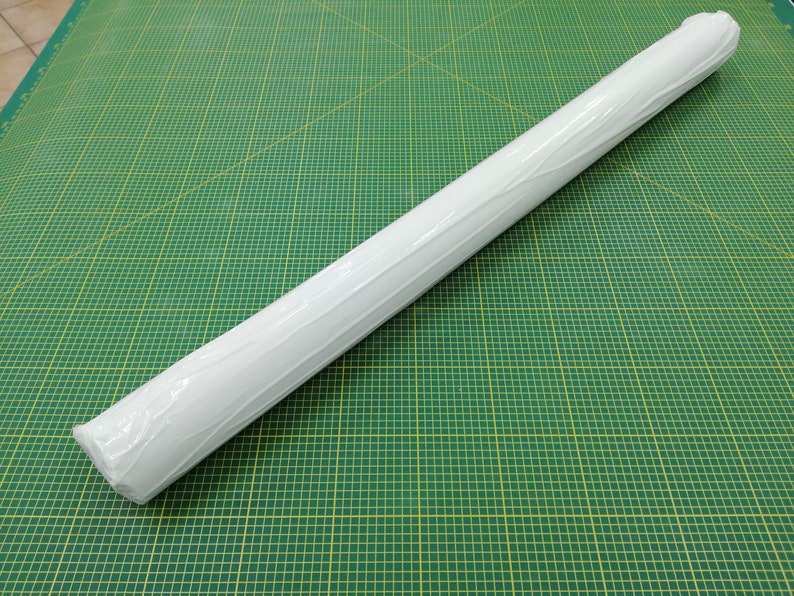 May include: A white roll of paper wrapped in clear plastic, sitting on a green cutting mat with yellow grid lines.