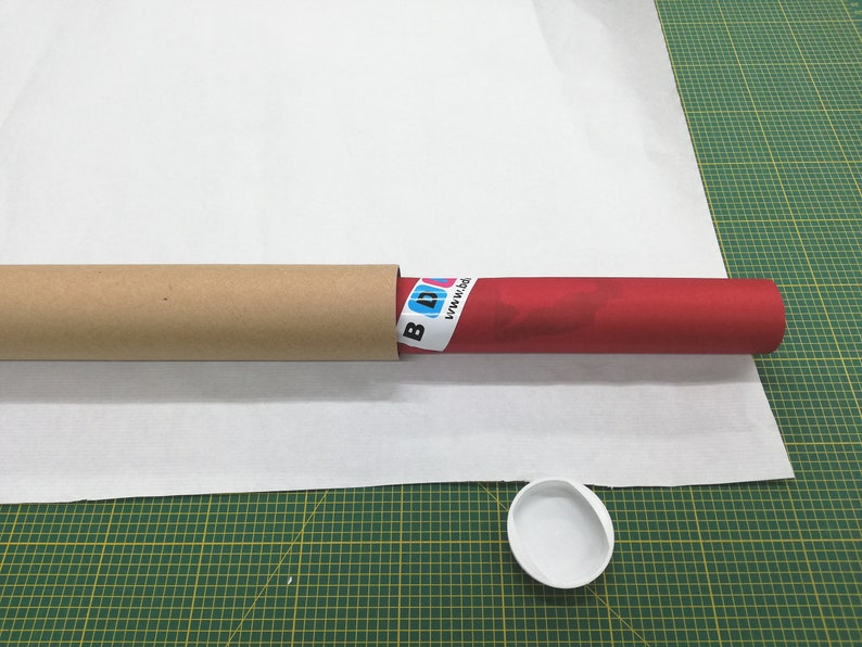 May include: A red poster tube with a white label that says "www.pixi.de" is inside a brown cardboard tube. A white plastic lid is on a green cutting mat.
