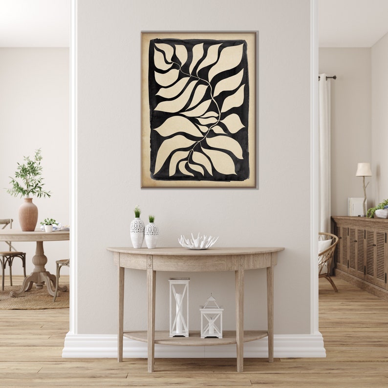 May include: Black and white abstract art print of stylized leaves. The print is framed and hanging on a white wall above a wooden console table.