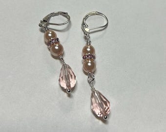 May include: A pair of dangle earrings featuring a combination of pink pearls, clear pink crystal teardrops, and silver-tone metal findings. The earrings have a lever-back closure and are designed for pierced ears.