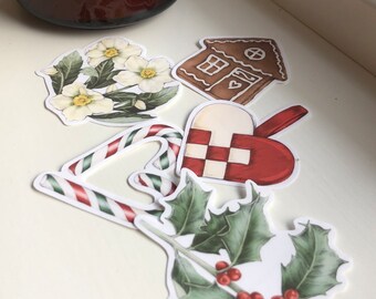 May include: A set of five Christmas-themed stickers featuring a gingerbread house, a candy cane, a holly sprig with red berries, a white flower, and a red and white heart.
