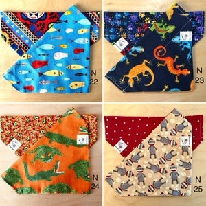 May include: Four different dog bandanas with various patterns. The bandanas are made of cotton fabric and have a triangular shape. The patterns include a blue bandana with fish, a navy bandana with lizards, an orange bandana with alligators, and a beige bandana with monkeys.