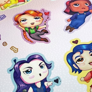 May include: A set of colorful cartoon character stickers featuring girls with different hairstyles and outfits. The stickers are printed on white paper with a light pink polka dot pattern. The text "EveningAlchemy on Etsy; Re" is visible at the bottom of the image.