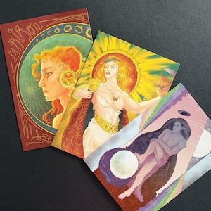 May include: Three illustrated cards with a fantasy theme. The first card features a woman with red hair and a blue eye, wearing a gold crown and a blue and gold dress. The second card features a woman with blonde hair and a blue eye, wearing a gold crown and a blue and gold dress. The third card features a man with blue hair and a blue eye, wearing a blue and gold dress. The cards are all set against a background of stars and moons.