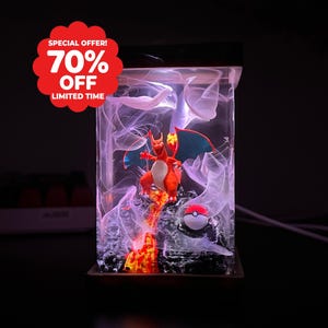 Könnte beinhalten: Eine rechteckige Harzlampe mit einer Glurak-Figur auf einem felsigen Sockel mit Flammeneffekt, einem kleinen Pokéball und wirbelnden, rauchartigen weißen Mustern im Inneren. Ein rotes Abzeichen zeigt den Text SPECIAL OFFER! 70% OFF LIMITED TIME.