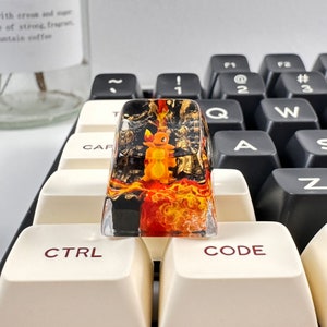 May include: A clear resin keycap with a black and orange design. The design features a cartoon character with a yellow body and orange flames. The keycap is labeled "CODE" in red.