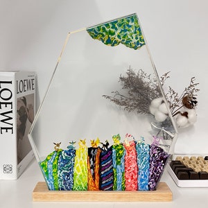 May include: A decorative acrylic art piece with a wooden base. The clear, geometric shape features a colorful, textured design at the bottom and a patterned top. The piece is displayed on a white surface.