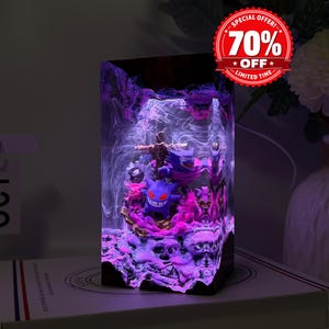 May include: A rectangular resin lamp featuring a purple Gengar character figurine encased within a clear block. The interior displays swirling white smoke-like patterns and pink lighting, with a textured base resembling rocky terrain.