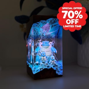 Peut inclure: Une lampe rectangulaire en résine et bois contenant trois figurines de tortues bleues, illuminée par une lueur bleue vive. Le coin supérieur droit affiche un badge festonné rouge avec le texte blanc SPECIAL OFFER! 70% OFF LIMITED TIME.