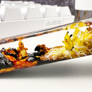 May include: A clear resin tube filled with colorful layers of resin, including black, orange, yellow, white, brown, and green.  The tube contains two small figurines, one yellow and one orange.