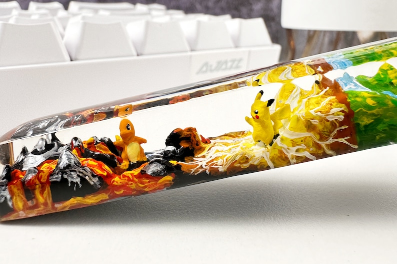 May include: A clear resin tube filled with colorful layers of resin, including black, orange, yellow, white, brown, and green.  The tube contains two small figurines, one yellow and one orange.