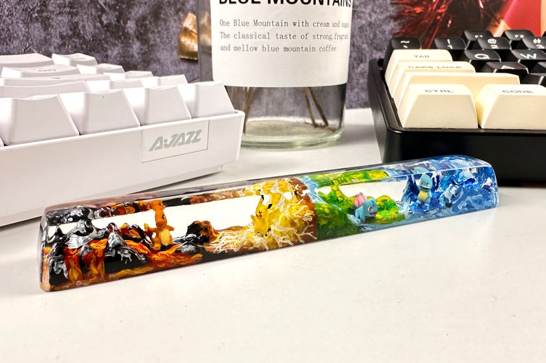 May include: A clear resin keyboard wrist rest with a multi-colored design featuring four different Pokemon characters. The wrist rest is divided into four sections, each with a different color and design. The first section is orange and black with a Charmeleon Pokemon character. The second section is yellow and white with a Pikachu Pokemon character. The third section is green and brown with a Bulbasaur Pokemon character. The fourth section is blue and white with a Squirtle Pokemon character.
