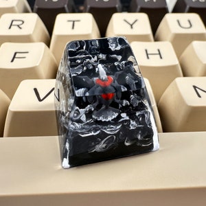 May include: A black and white marbled keyboard keycap with a red and white design inside. The keycap is sitting on a beige keyboard.